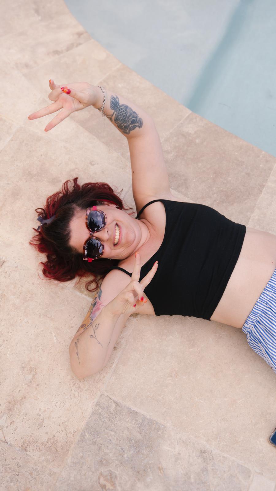 Maud, allongée au bord d'une piscine, sourit et fait le signe de la paix